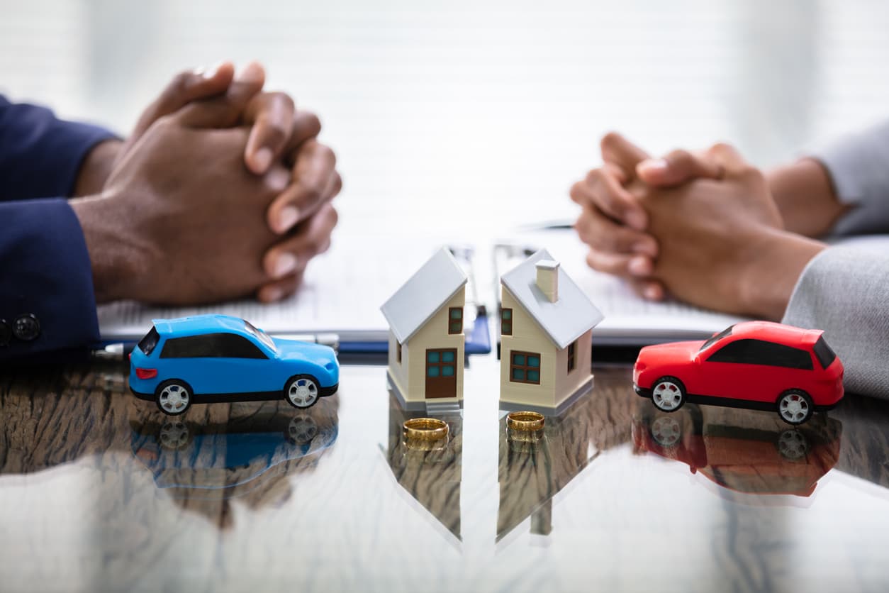 Husband and wife sit contempalting division of assets with two toy cars and a split model house