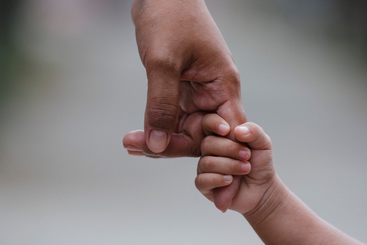 A child grips their father's finger with their hand